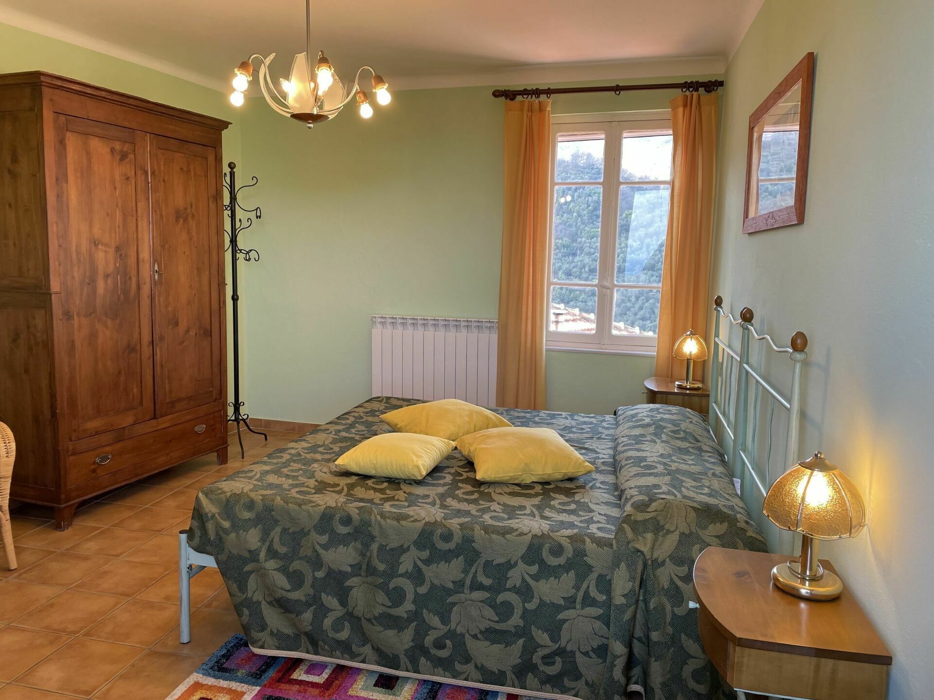 A bedroom with a bed, a wardrobe, a radiator, a window with curtains, a bedside lamp, and a mirror.