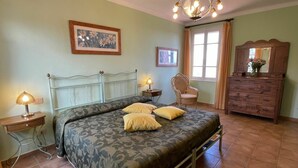 Ein Schlafzimmer mit Bett, Nachttischlampen, einem Sessel, einem Schminktisch und einem Fenster mit Vorhängen.