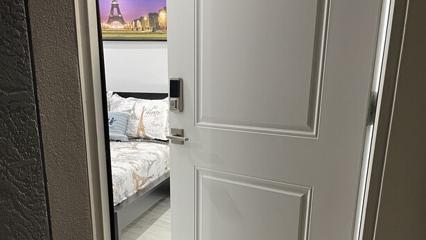 En hotelindgang med en hvid dør, en dørmåtte og en seng med udsigt til Eiffeltårnet.