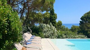 A poolside area with lounge chairs and a table, surrounded by greenery and overlooking the sea. - Casa Blue Art by Interhome (Pals)