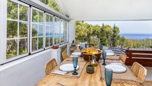 A dining area with a table set for four, large windows, and a view of the sea. - Casa Blue Art by Interhome (Pals)