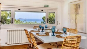 A dining area with a view of the sea, white walls, and wicker chairs. - Casa Blue Art by Interhome (Pals)