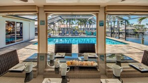 Ein Essbereich mit Glastisch und Blick auf einen Pool, ausgestattet mit Stühlen und Besteck.