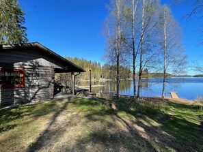 Una baita con un molo che si protende in un lago, circondata da alberi e un cielo sereno.