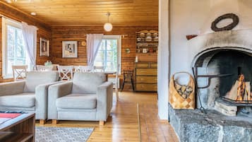 A cozy cabin interior with a fireplace, wooden walls, and a dining area.