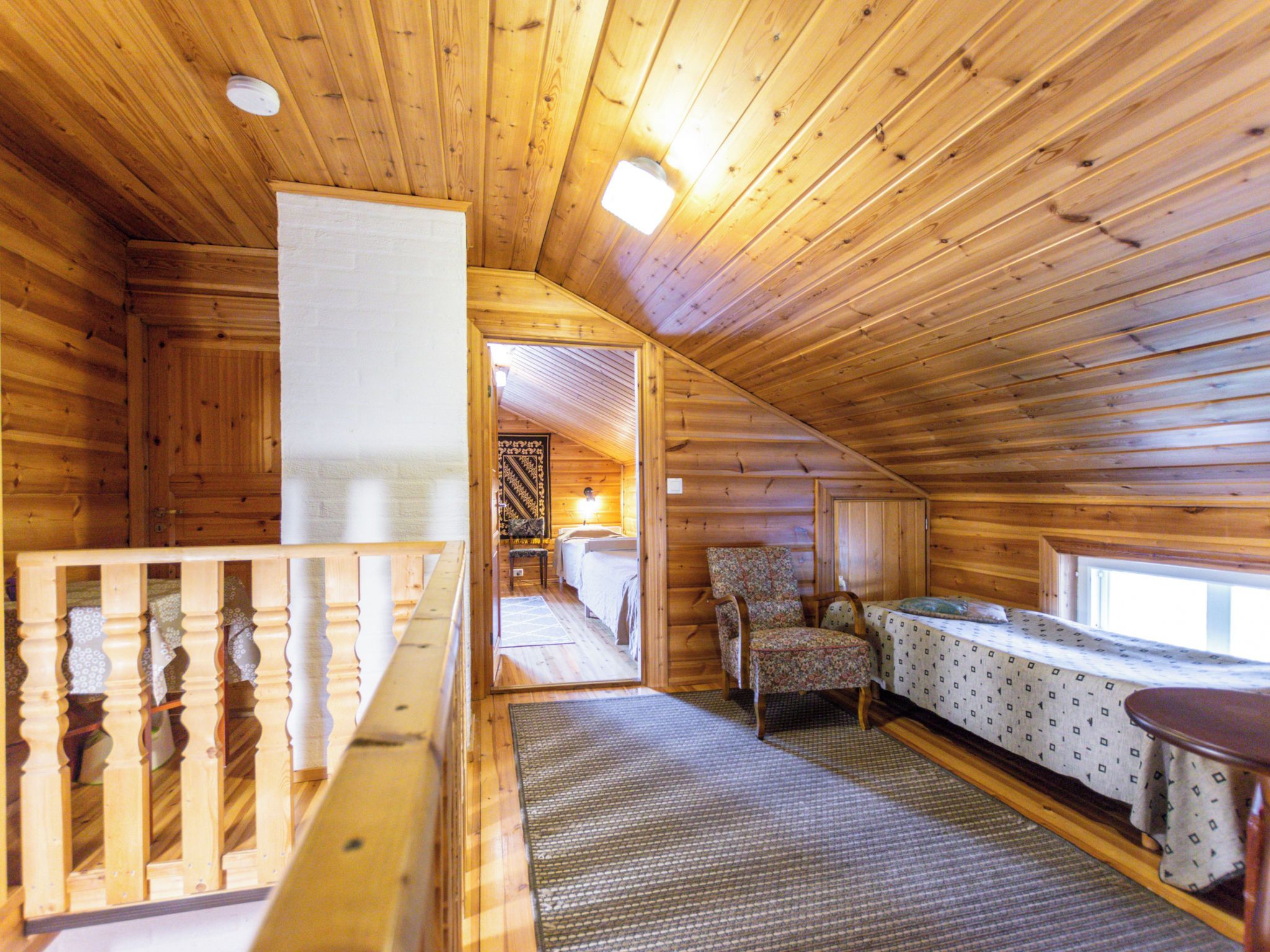 A wooden interior with a balcony, a bed, a chair, and a table.