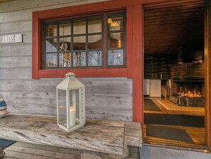 A wooden exterior with a red-framed window, a white lantern, and a visible fireplace inside.