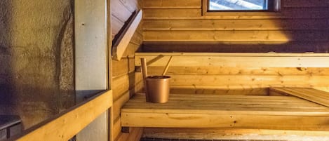 Eine Sauna mit Holzbänken und einem Metallkübel.