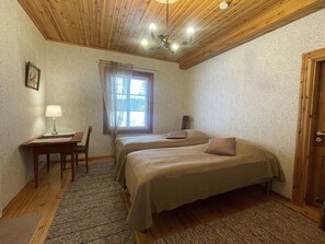 A room with two beds, a desk, a chair, a lamp, and a window with curtains.