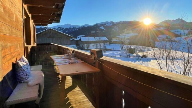 Eine Holzterrasse mit Tisch und Bank, mit Blick auf eine verschneite Landschaft und Berge.