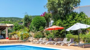 A swimming pool with lounge chairs and umbrellas, surrounded by greenery and a building. - El Suro by Interhome (Calonge)