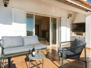 A balcony with a sofa, a chair, and a small table with a bottle and glasses. - El Suro by Interhome (Calonge)