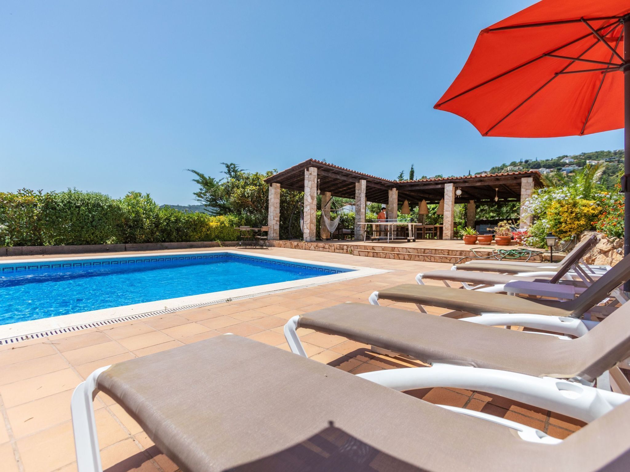 A pool area with lounge chairs, a pergola, and a view of the surrounding landscape.