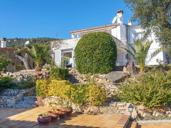 A white building with a stone facade, a stone wall with greenery, and a tiled patio area.