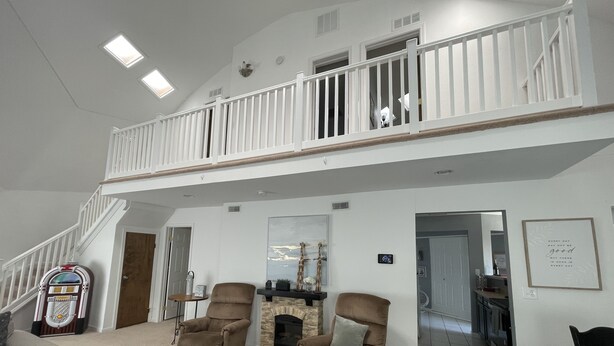 A spacious living room with a high ceiling, a fireplace, a staircase leading to an upper level, and a view of the kitchen. - THUNDERDOME (awesome Dome House) Unique home with Beautiful views/Comfy and Cozy (Erie)