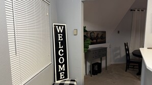 A hallway with a 'WELCOME' sign, a bench, a dining area with a table and chairs, and a small cabinet. - THUNDERDOME (awesome Dome House) Unique home with Beautiful views/Comfy and Cozy (Erie)