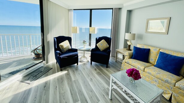 A spacious room with a balcony overlooking the sea, featuring two armchairs, a sofa, and a coffee table. - Oceanfront Condo in Garden City Beach!!!! (murrells inlet)
