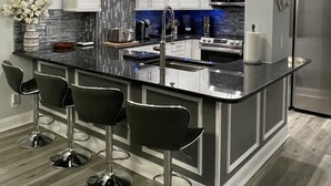 A modern kitchen with a central island, bar stools, stainless steel appliances, and a decorative backsplash. - Oceanfront Condo in Garden City Beach!!!! (murrells inlet)