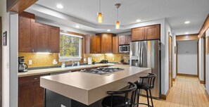A modern kitchen with wooden cabinets, a central island, bar stools, and stainless steel appliances.
