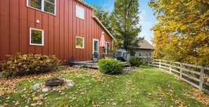 Une maison rouge avec une terrasse, un barbecue et une clôture blanche.