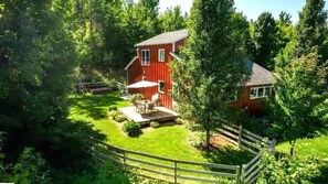 A red house surrounded by lush greenery, with a wooden deck and a small patio area. - Red Timbers Near Beaches and Wineries (Traverse City)