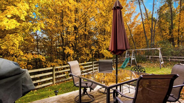 Un patio con mobiliario exterior, un conjunto de columpios y una terraza de madera.