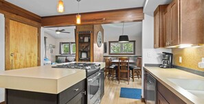 A modern kitchen with a central island, wooden cabinets, a built-in oven, and a dining area with a chandelier.