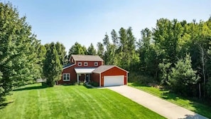Ein zweistöckiges Haus mit Garage, umgeben von einem gepflegten Rasen und dichtem Wald.