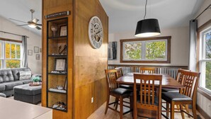 Una sala de estar moderna con un muro decorativo de madera, una mesa de comedor con sillas, un sofá y un ventilador de techo.