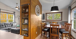 Un salon moderne avec un mur d’accent en bois, une table à manger avec des chaises, un canapé et un ventilateur de plafond.