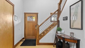 Un pasillo con puerta de madera, una escalera con barandilla de madera, un letrero de bienvenida, un mapa enmarcado y un escritorio con una planta.
