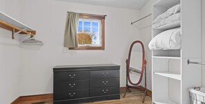 Un dormitorio con un aparador de madera, un tocador con espejo, una ventana con cortina y un armario con repisas.