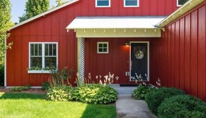 A red single-story house with a front porch, a black door, and a small garden with various plants.
