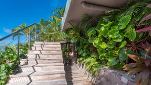 A wooden staircase leading up to a building, surrounded by lush tropical plants and a clear blue sky. - Villa Bayugita | Ocean View - Located in  Exquisite Pointe Milou with Private Pool (Pointe Milou)