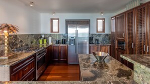 A modern kitchen with granite countertops, stainless steel appliances, wooden cabinets, and a central island. - Villa Bayugita | Ocean View - Located in  Exquisite Pointe Milou with Private Pool (Pointe Milou)