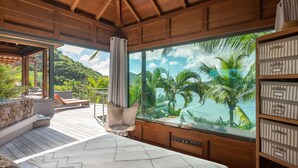 A bedroom with a large window, wooden ceiling, and a view of palm trees and a beach. - Villa Bayugita | Ocean View - Located in  Exquisite Pointe Milou with Private Pool (Pointe Milou)