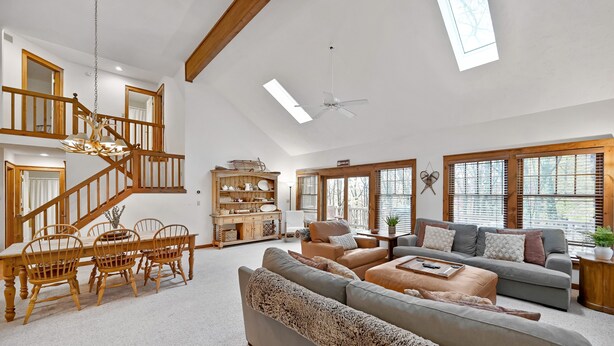 Ein geräumiges Wohnzimmer mit hoher Decke, einer Holztreppe und großen Fenstern.