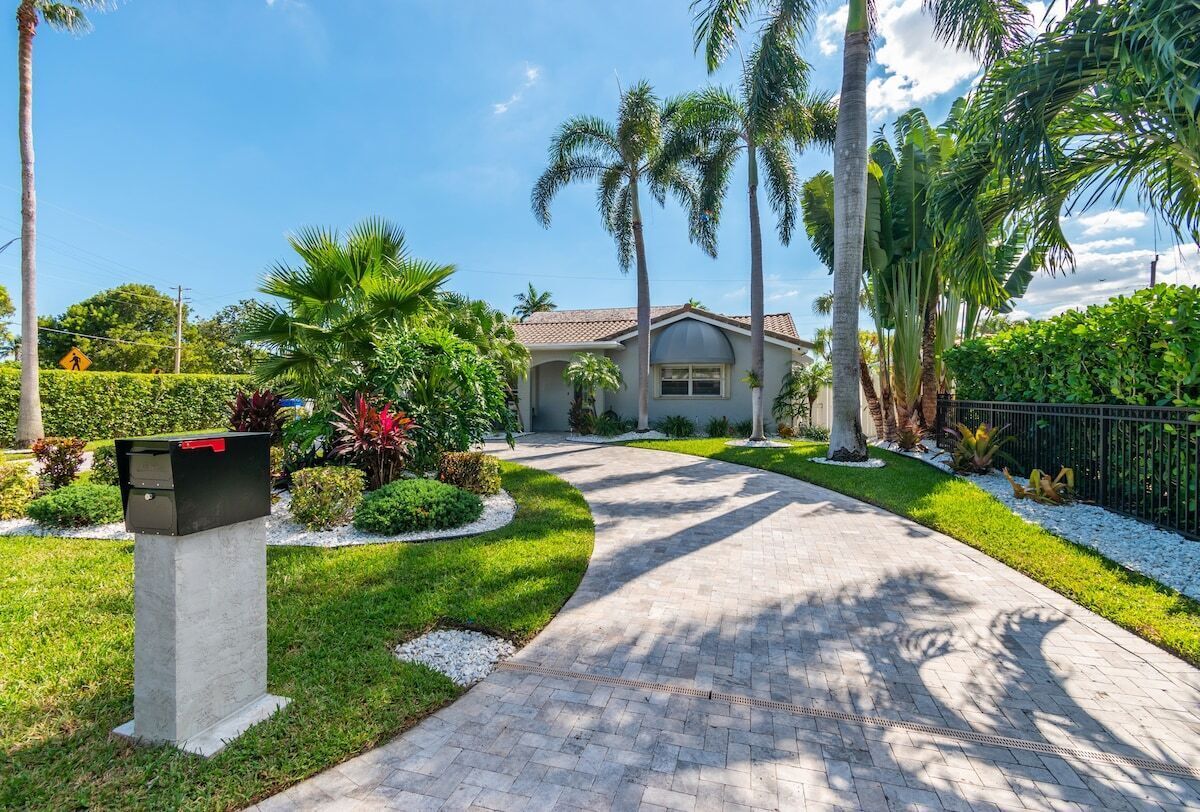 A residential property with a paved driveway, palm trees, and a mailbox.
