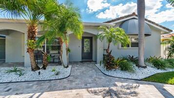 A residential house with a paved driveway, palm trees, and a well-maintained garden.