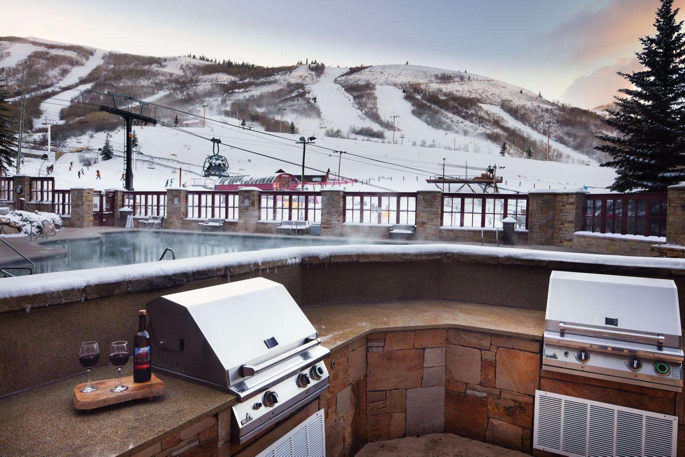 An outdoor barbecue area with stone walls, a grill, and a hot tub.