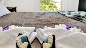 Una cama con cubrecolor en tono marrón texturizado, almohadas blancas y vistas al verdor a través de una ventana.