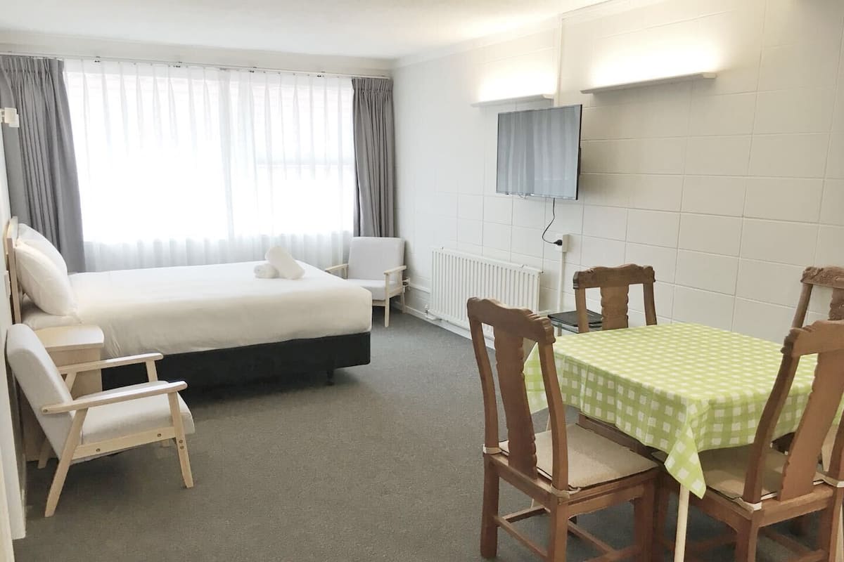 Una habitación de hotel con una cama, una silla, una mesa con mantel a cuadros y un televisor instalado en la pared.