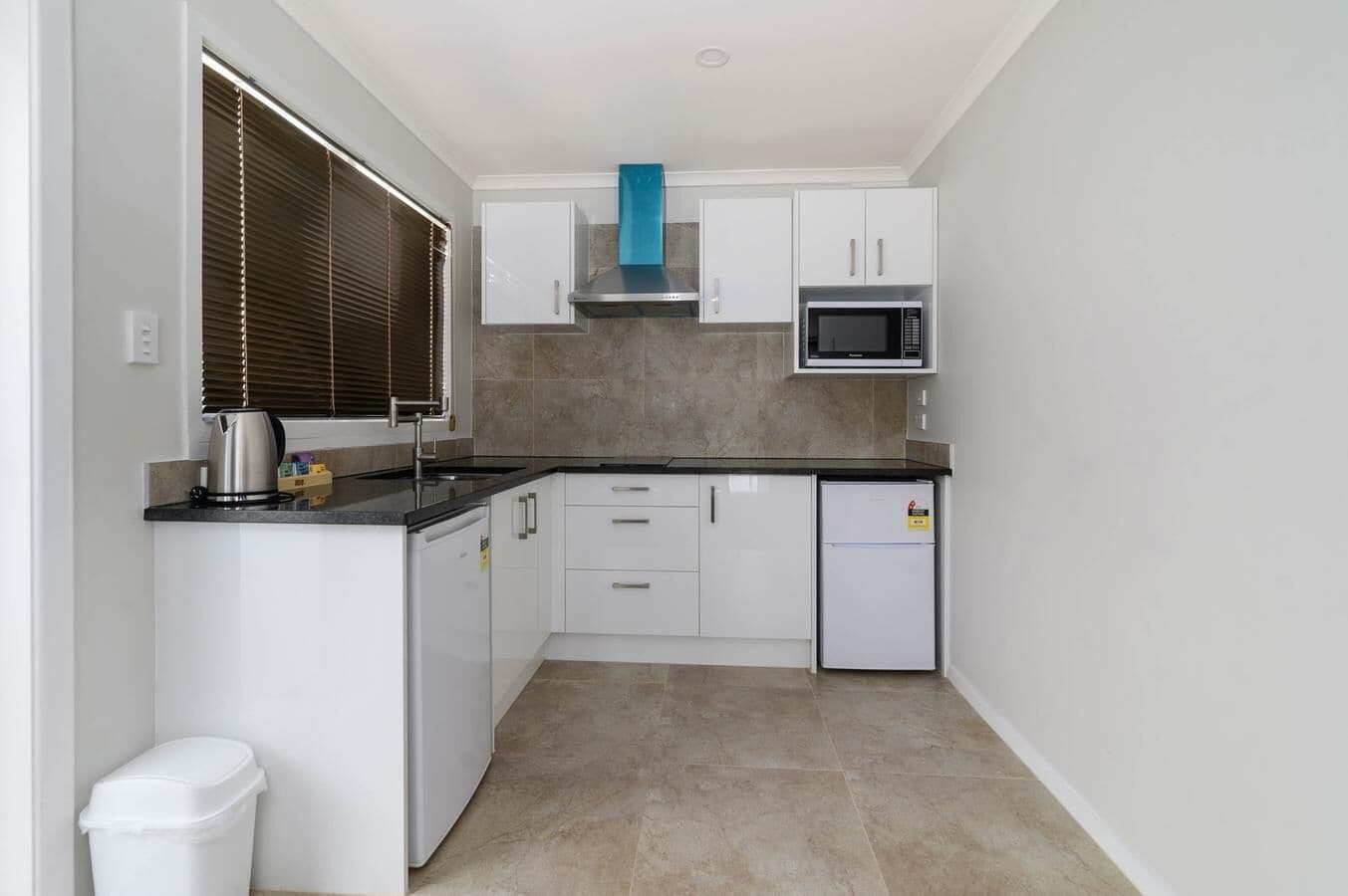 Una cocina compacta con armarios blancos, un microondas, una estufa y un cubo de basura.