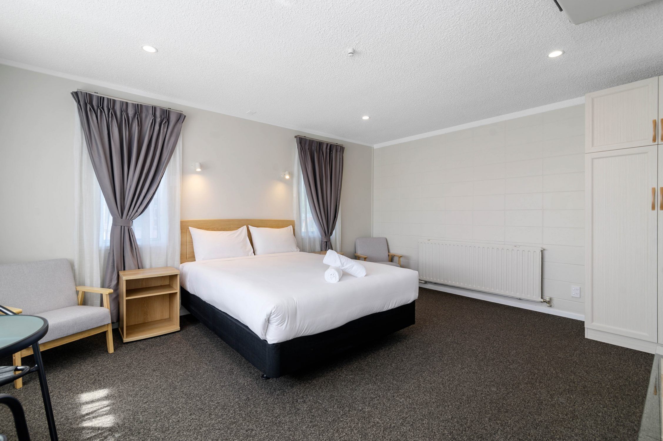 A hotel room with a bed, a chair, a small table, and a wardrobe.