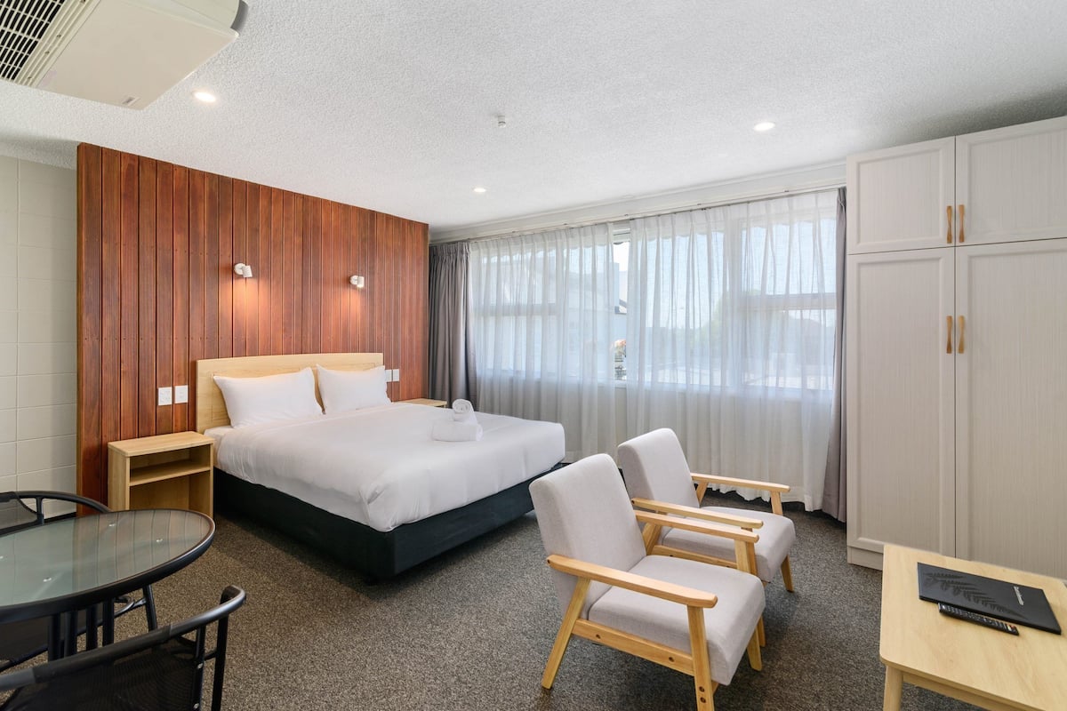 Habitación de hotel con cama, dos sillones, una mesita, armario y ventana con cortinas.