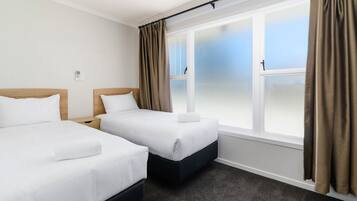 A hotel room with two single beds, a large window with curtains, and a carpeted floor.