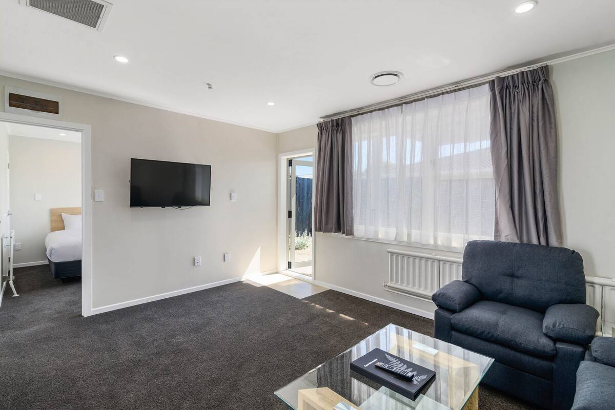 Una sala de estar moderna con una televisión de pantalla plana, un sofá gris y una mesa de centro de vidrio.