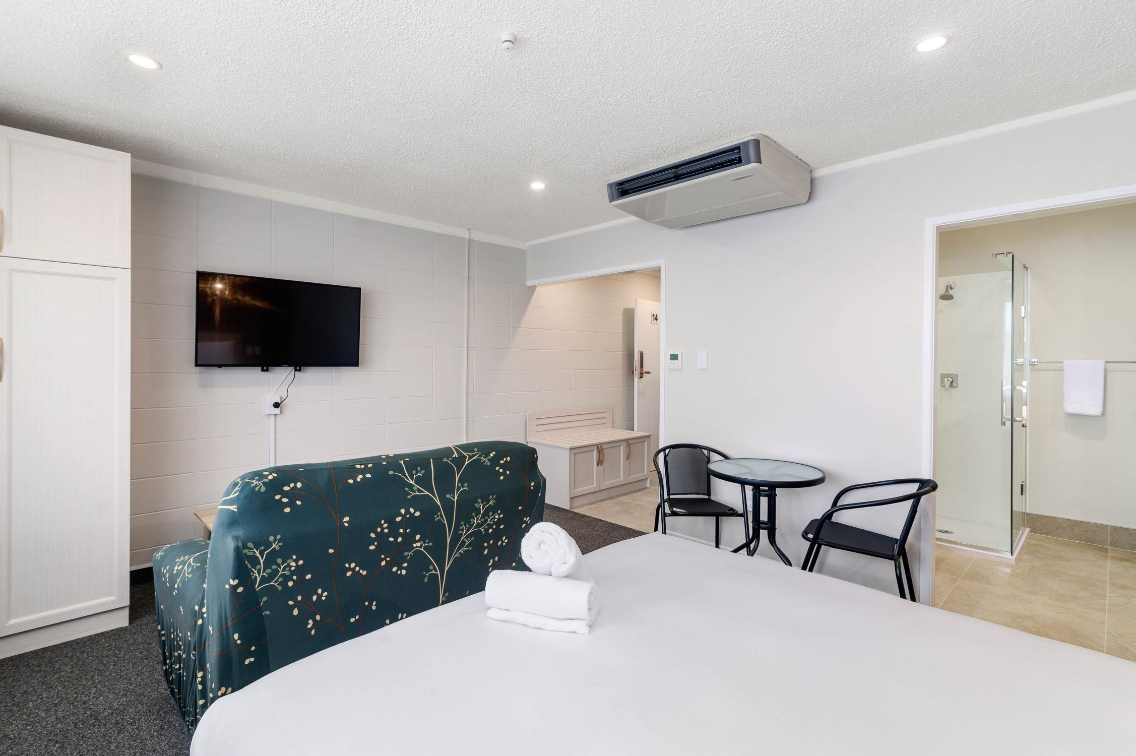 Habitación de hotel con cama, televisión, una mesita con sillas y zona de ducha.