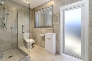 A modern bathroom with a glass-enclosed shower, a toilet, a sink, and a frosted glass door. - Thermal Oak Motel (Rotorua)