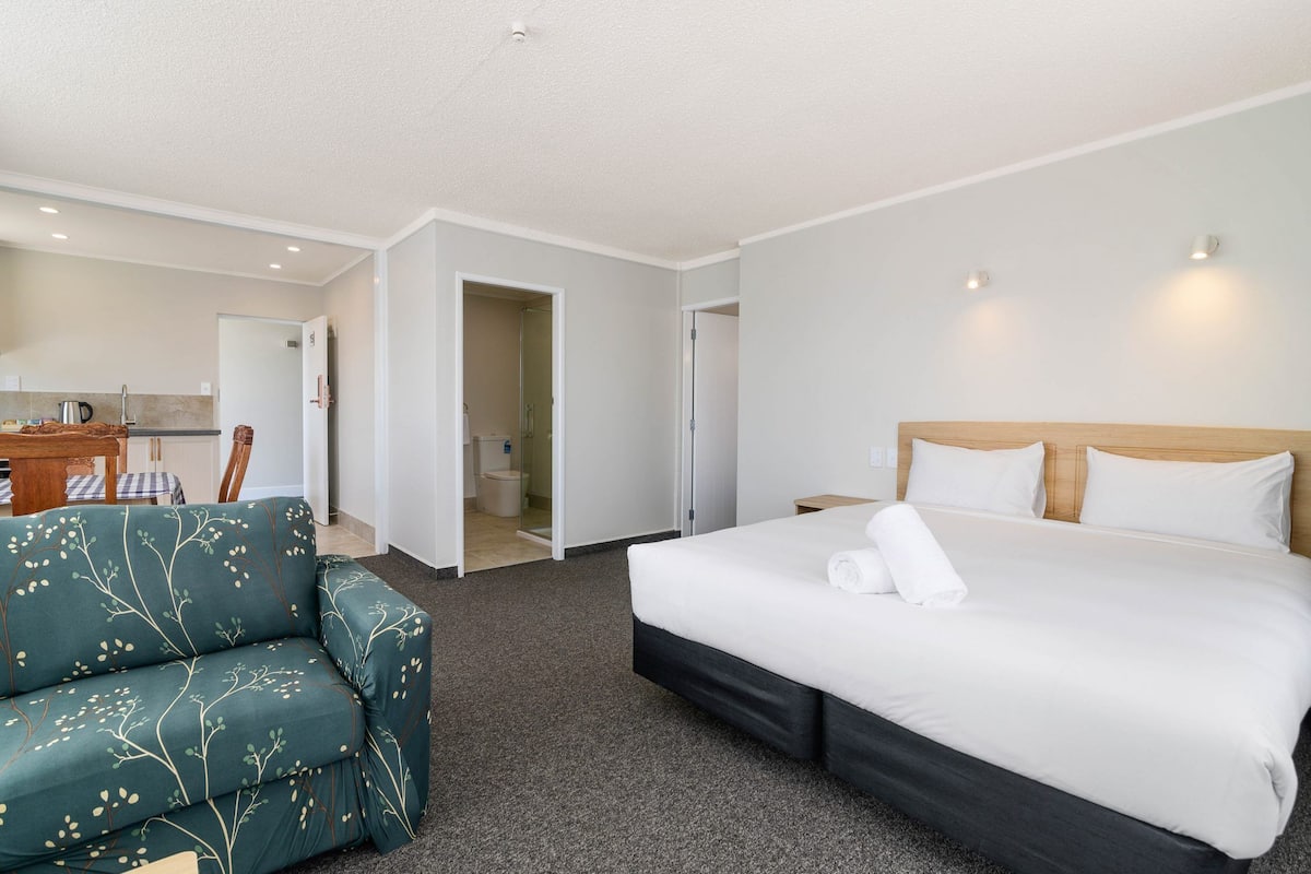 Una habitación de hotel con cama, sofá, una mesita y una kitchenette.